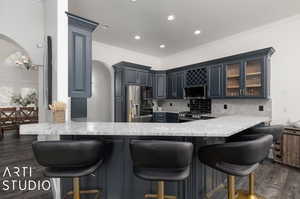 Kitchen with dark hardwood / wood-style flooring, kitchen peninsula, stainless steel appliances, tasteful backsplash, and crown molding