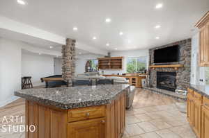 Kitchen with a stone fireplace, light tile flooring, and a kitchen island