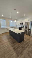 Kitchen with a center island, stainless steel appliances, white cabinets, and wood-type flooring