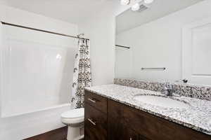 Full bathroom with vanity with extensive cabinet space, hardwood / wood-style flooring, toilet, and shower / tub combo with curtain