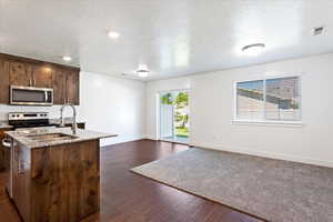 Kitchen featuring stainless steel appliances, light stone counters, sink, and dark wood-type flooring