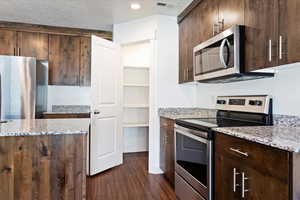 Kitchen featuring light stone countertops, dark brown cabinets, dark hardwood / wood-style flooring, and appliances with stainless steel finishes