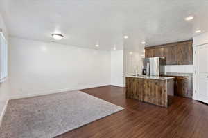 Kitchen featuring stainless steel fridge, a textured ceiling, dark hardwood / wood-style floors, and a kitchen island with sink