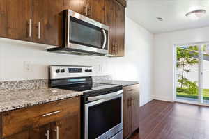 Kitchen with dark hardwood / wood-style floors, light stone countertops, and stainless steel appliances