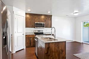 Kitchen featuring dark hardwood / wood-style floors, stainless steel appliances, light stone countertops, sink, and a textured ceiling