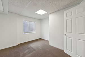 Empty room featuring dark carpet and a paneled ceiling