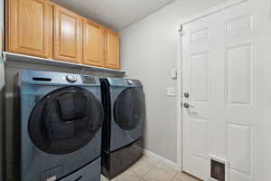 Clothes washing area featuring separate washer and dryer, cabinets, and light tile floors