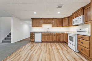 Kitchen featuring light stone countertops, a paneled ceiling, white appliances, sink, and light colored carpet