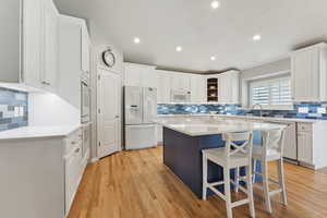 Kitchen with white cabinets, light hardwood / wood-style floors, a center island, and white appliances