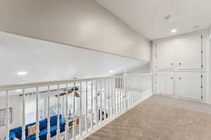 Corridor with vaulted ceiling and light colored carpet