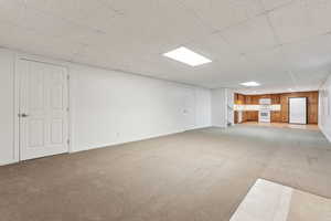 Basement featuring white refrigerator, a paneled ceiling, and carpet floors