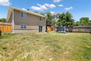 Back of house with a lawn and a trampoline