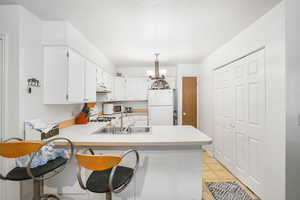 Kitchen with white cabinetry, white refrigerator, kitchen peninsula, sink, and light tile flooring