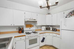 Kitchen with white cabinetry, white appliances, and light tile floors