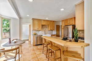 Kitchen featuring a textured ceiling, backsplash, light tile floors, and stainless steel appliances