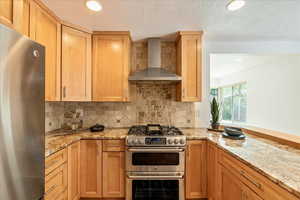 Kitchen featuring stainless steel appliances, wall chimney range hood, tasteful backsplash, and a textured ceiling