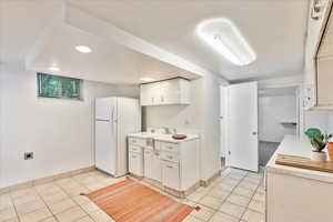 Kitchen featuring white cabinets, white fridge, and light tile floors