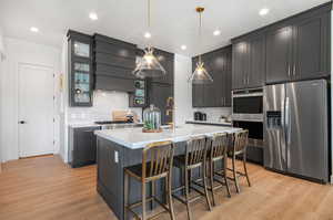 Kitchen featuring light hardwood / wood-style floors, custom range hood, a center island with sink, stainless steel appliances, and backsplash