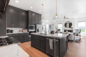 Kitchen with light wood-type flooring, appliances with stainless steel finishes, a kitchen island with sink, sink, and tasteful backsplash