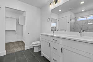 Bathroom with double sink, vanity with extensive cabinet space, tile floors, a wealth of natural light, and toilet