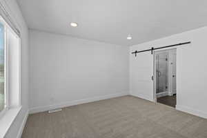 Unfurnished bedroom with a barn door, dark colored carpet, and ensuite bath