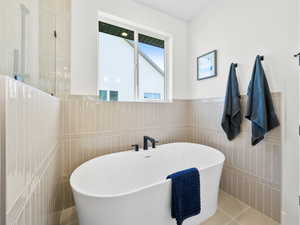 Bathroom with a bathtub, tile patterned flooring, and tile walls