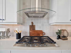 Kitchen with wall chimney exhaust hood, decorative backsplash, light stone countertops, and white cabinets