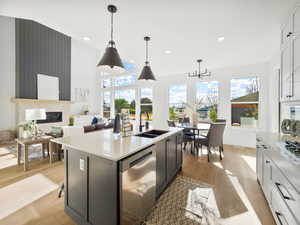 Kitchen with light wood-type flooring, a kitchen island with sink, dishwasher, sink, and decorative light fixtures