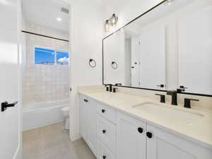 Full bathroom featuring toilet, double vanity, tiled shower / bath combo, and tile patterned floors