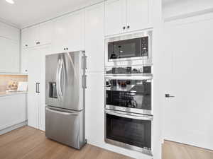 Kitchen with light wood-type flooring, appliances with stainless steel finishes, decorative backsplash, and white cabinets