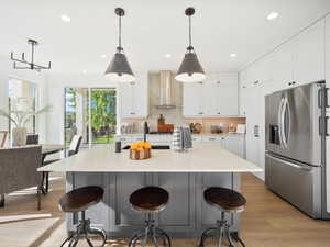 Kitchen with stainless steel refrigerator with ice dispenser, tasteful backsplash, wall chimney exhaust hood, and decorative light fixtures