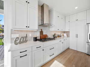 Kitchen featuring appliances with stainless steel finishes, light hardwood / wood-style floors, white cabinetry, tasteful backsplash, and wall chimney range hood