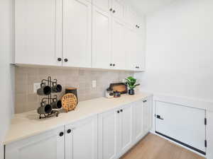 Bar with white cabinets, decorative backsplash, and light wood-type flooring