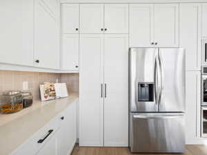 Kitchen featuring light wood-type flooring, light stone countertops, tasteful backsplash, white cabinetry, and stainless steel appliances