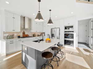 Kitchen with wall chimney range hood, light wood-type flooring, tasteful backsplash, appliances with stainless steel finishes, and sink