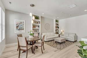 Dining space with a textured ceiling, built in shelves, and light hardwood / wood-style flooring