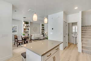 Kitchen featuring light hardwood / wood-style flooring, decorative light fixtures, built in features, a kitchen island, and white cabinets