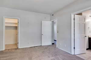 Unfurnished bedroom featuring light carpet, a walk in closet, and a closet