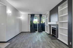 Unfurnished living room featuring built in shelves and hardwood / wood-style floors