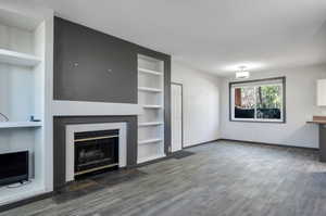 Unfurnished living room with built in shelves and dark hardwood / wood-style floors