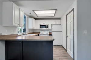 Kitchen featuring white cabinetry, light hardwood / wood-style flooring, white appliances, kitchen peninsula, and sink