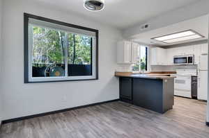 Kitchen with kitchen peninsula, white cabinets, white appliances, and light wood-type flooring