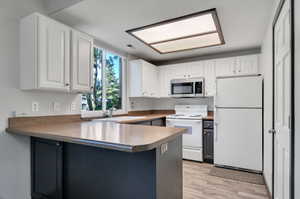 Kitchen featuring white cabinets, sink, kitchen peninsula, and white appliances