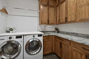 Clothes washing area with washer and clothes dryer, cabinets, sink, and dark tile floors