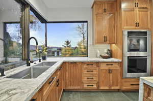 Kitchen with light stone countertops, double oven, backsplash, sink, and dark tile flooring