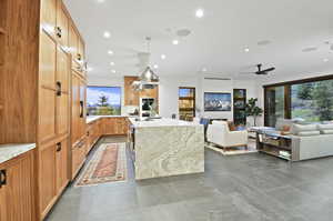 Kitchen with island exhaust hood, hanging light fixtures, ceiling fan, a center island, and dark tile flooring