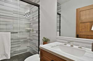 Bathroom featuring a shower with shower door, vanity, and toilet