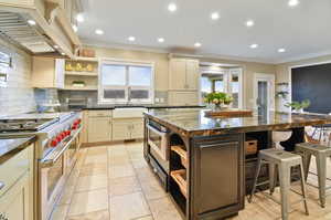 Kitchen featuring a kitchen island, custom range hood, stainless steel appliances, backsplash, and sink