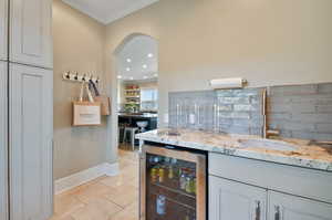 Kitchen with light stone countertops, ornamental molding, beverage cooler, backsplash, and sink