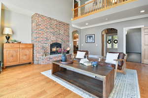 Living room with crown molding, brick wall, light hardwood / wood-style flooring, a brick fireplace, and a towering ceiling